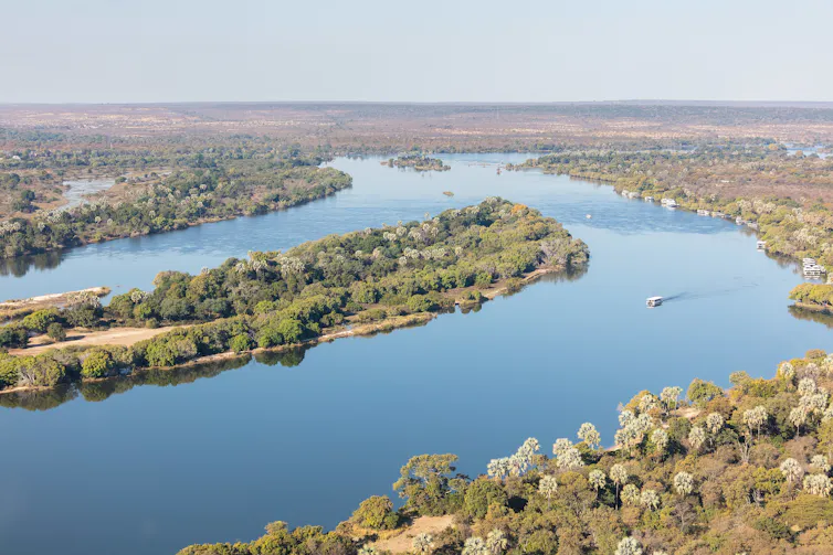 An aerial view of a vast river with a boat on it, wilds all around it.