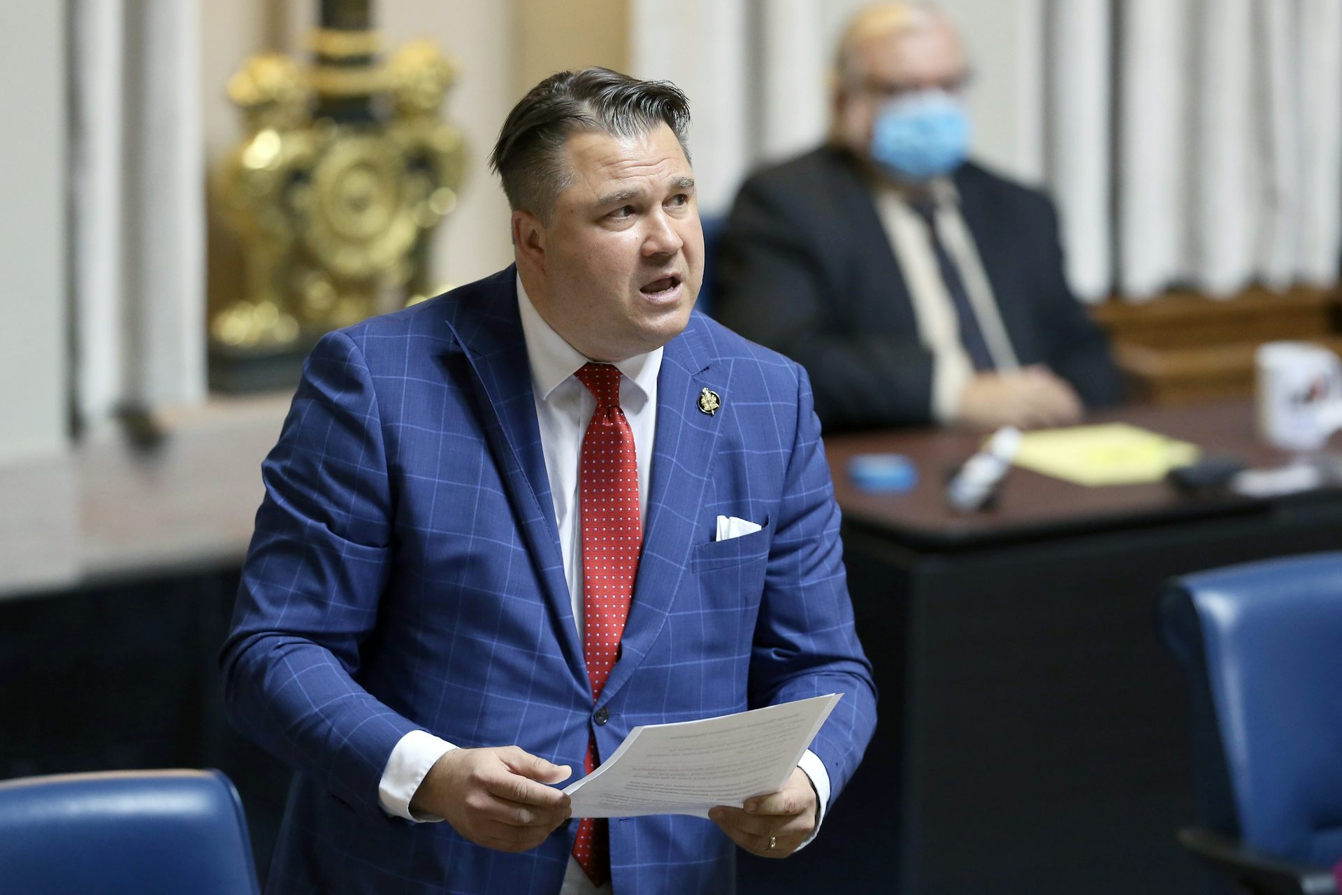 A man in a blue suit and short dark hair speaks in the Manitoba legislature.