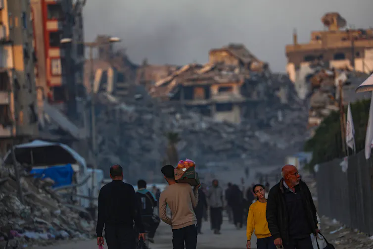 Palestinians walk among the rubble of destroyed buildings.