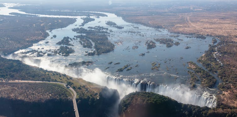 An aerial shot showing a vast river and a huge waterfall, spray rising.