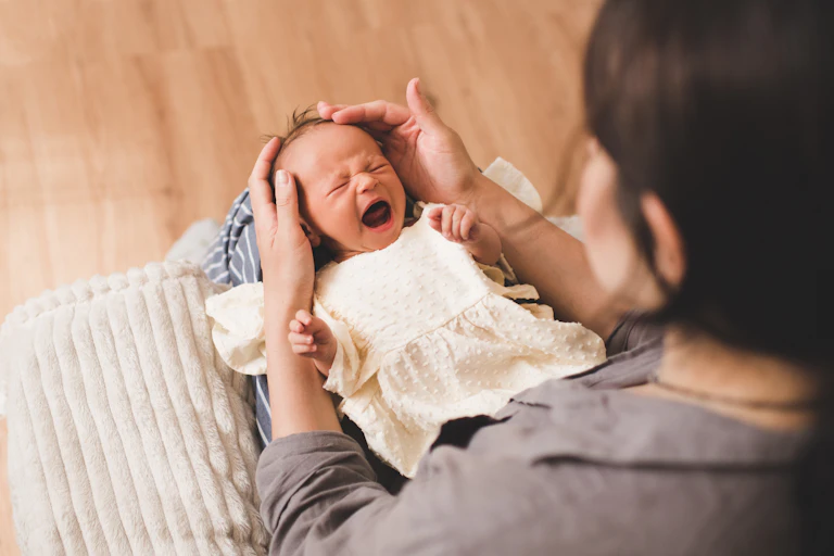 Un bébé en pleurs est posé sur les genoux de sa mère.