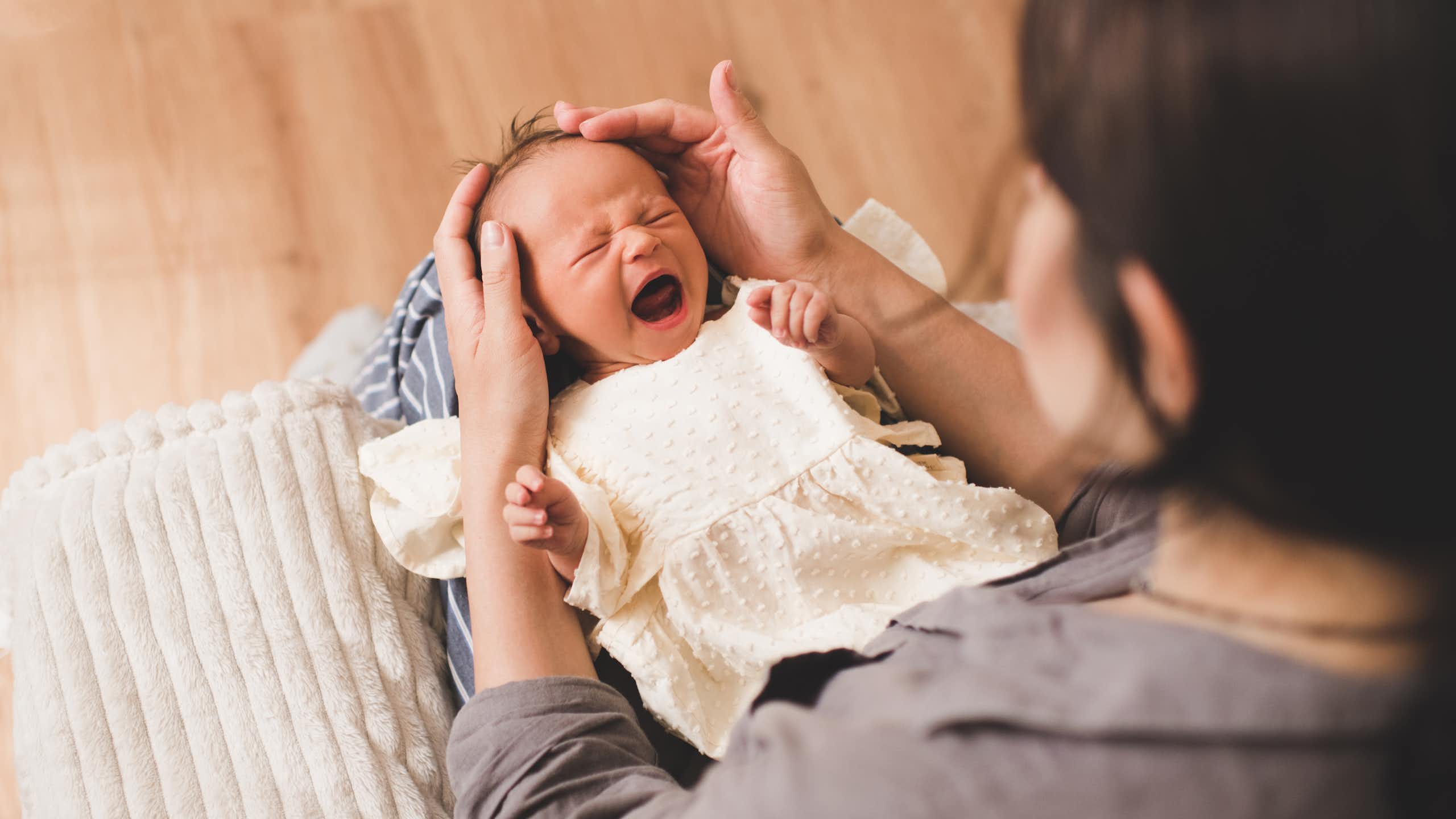Un bébé en pleurs est posé sur les genoux de sa mère.