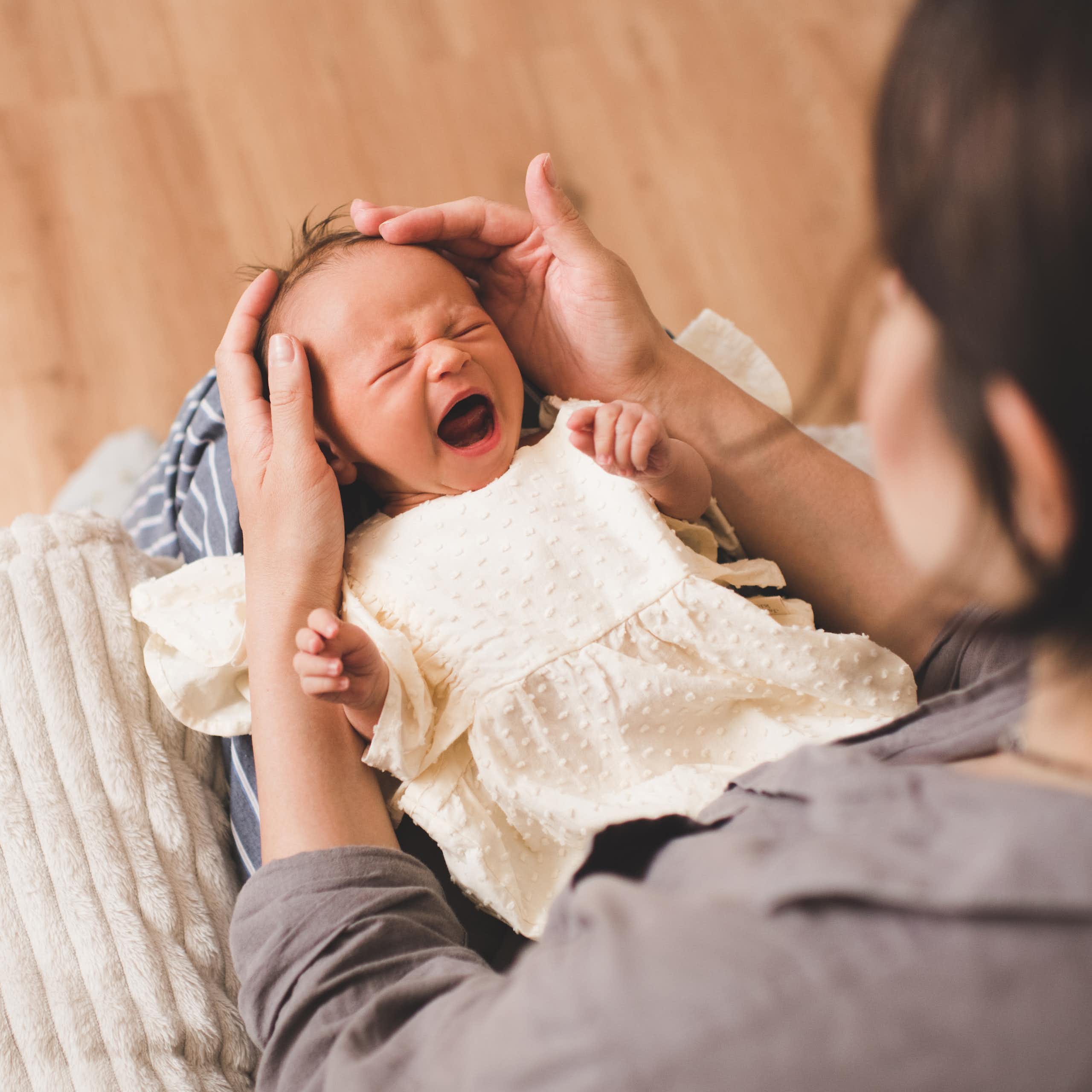 Un bébé en pleurs est posé sur les genoux de sa mère.