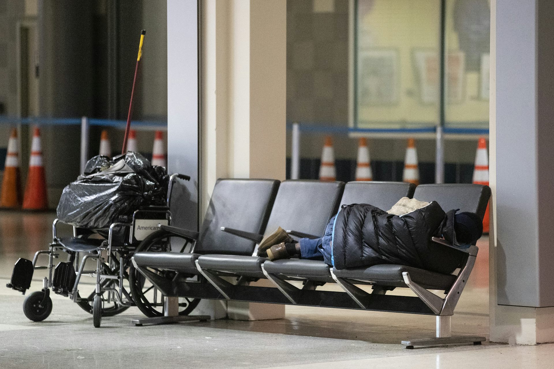 Person sleeps on chairs with wheelchair nearby