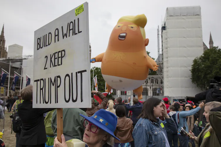 An inflatable caricature of Donald Trump is held aloft during a protest.