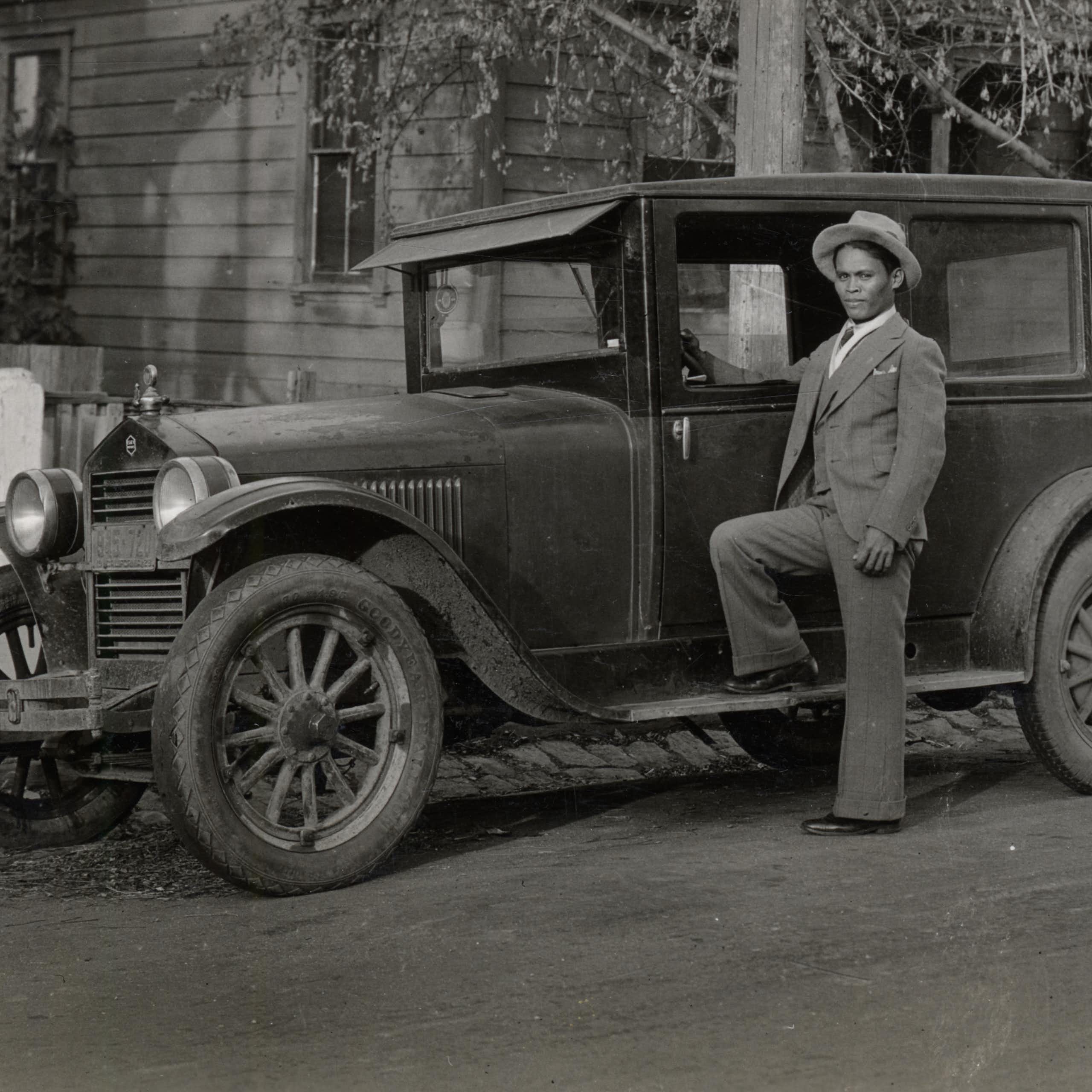 A young Filipino man poses next to his car in a vintage black and white photograph.