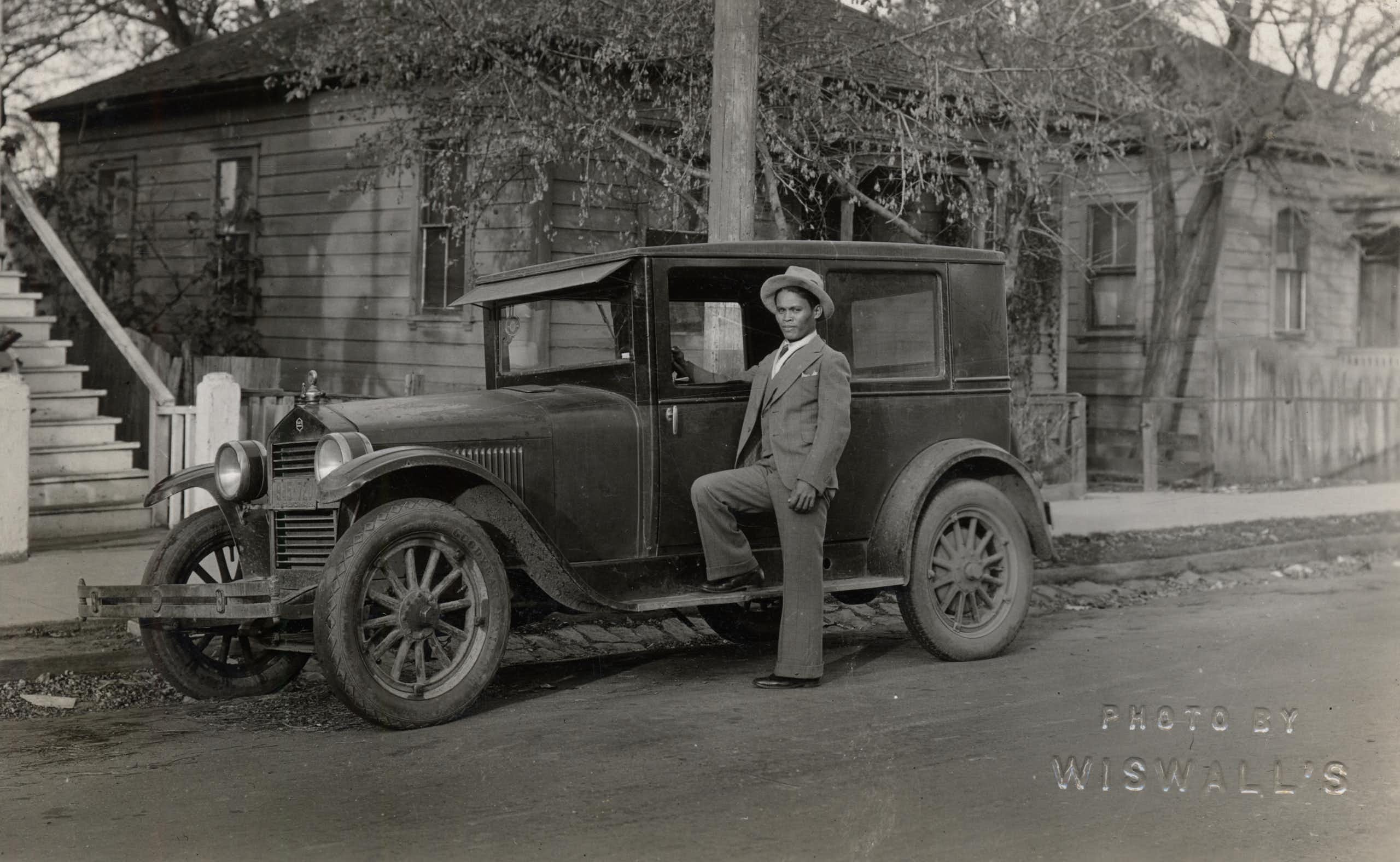 A young Filipino man poses next to his car in a vintage black and white photograph.