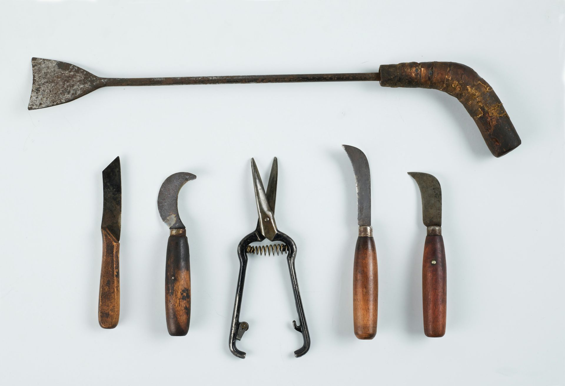 A collection of old, metal tools and knives laid out against a white backdrop.