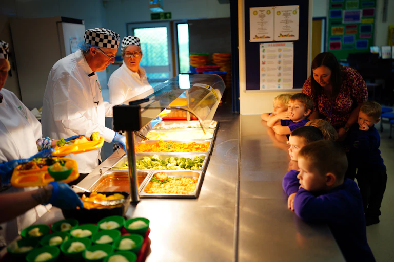Children look at food being served as part of a school lunch program