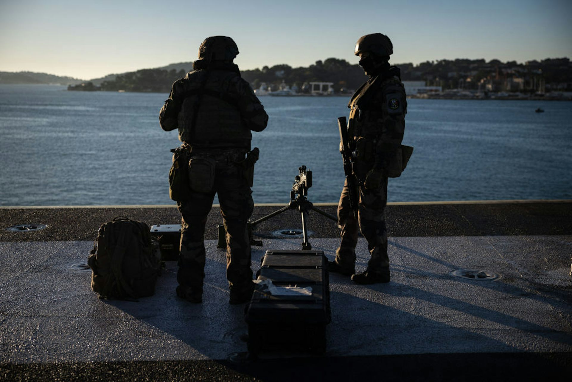 Two armed men standing on a raised platform and looking out into a large body of water.