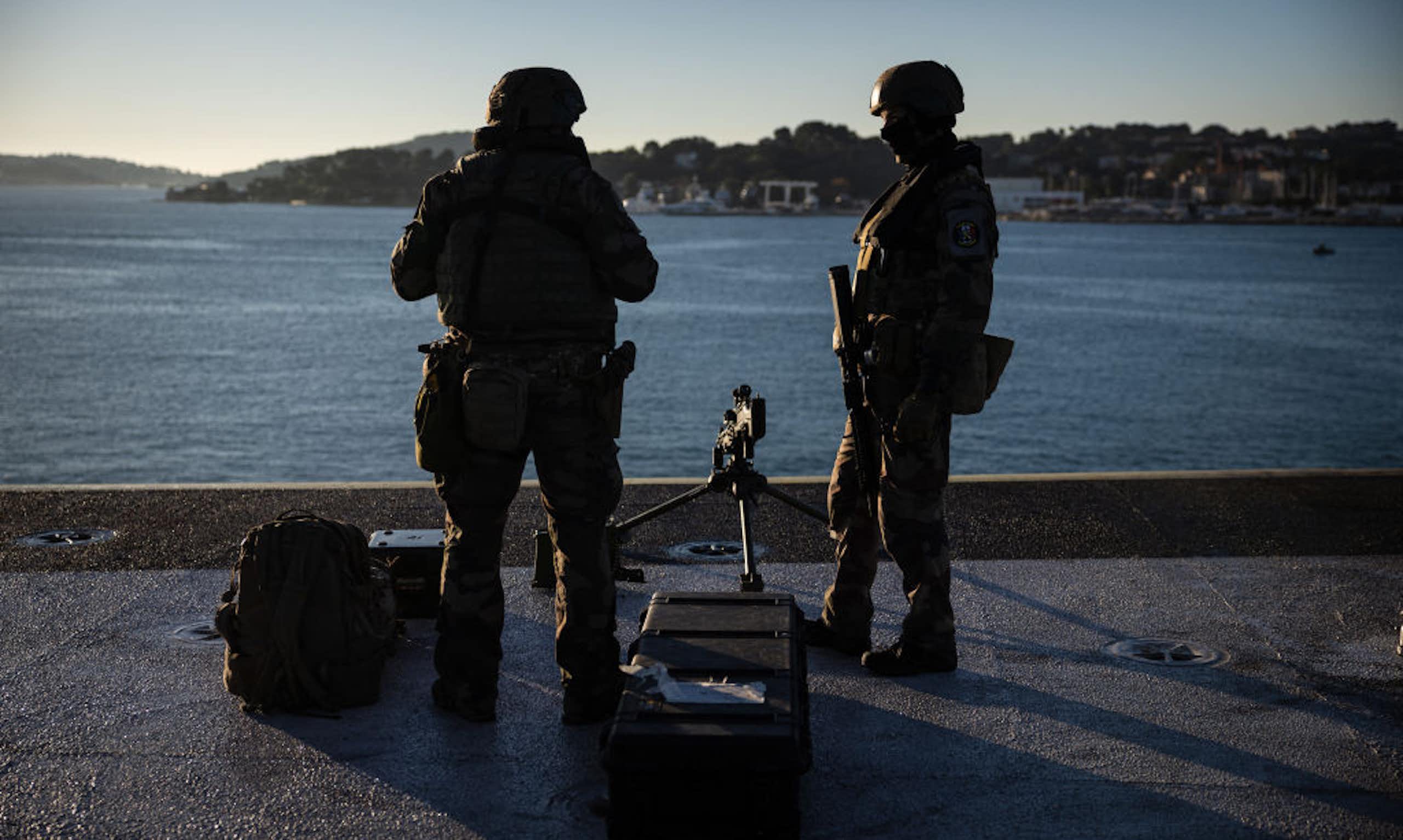 Two armed men standing on a raised platform and looking out into a large body of water.