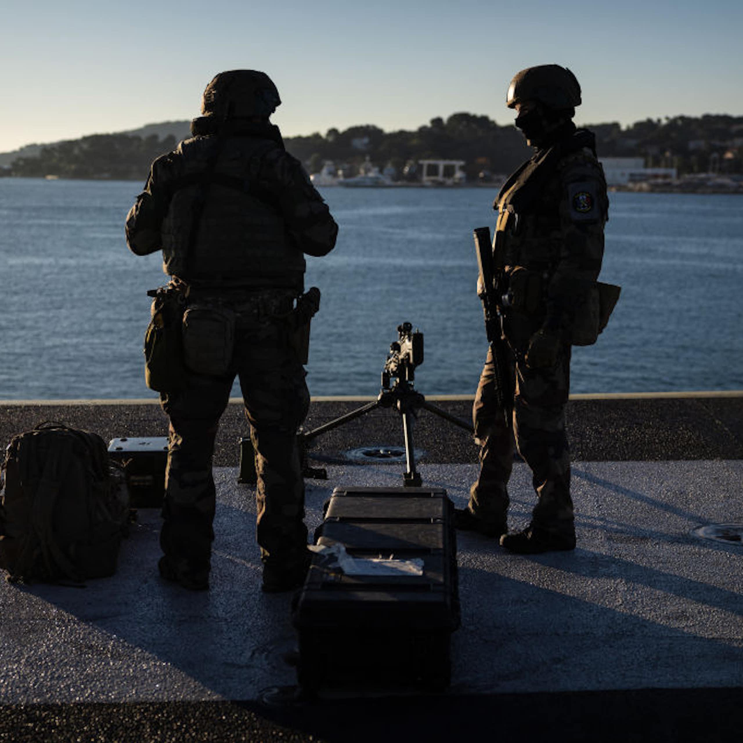 Two armed men standing on a raised platform and looking out into a large body of water.