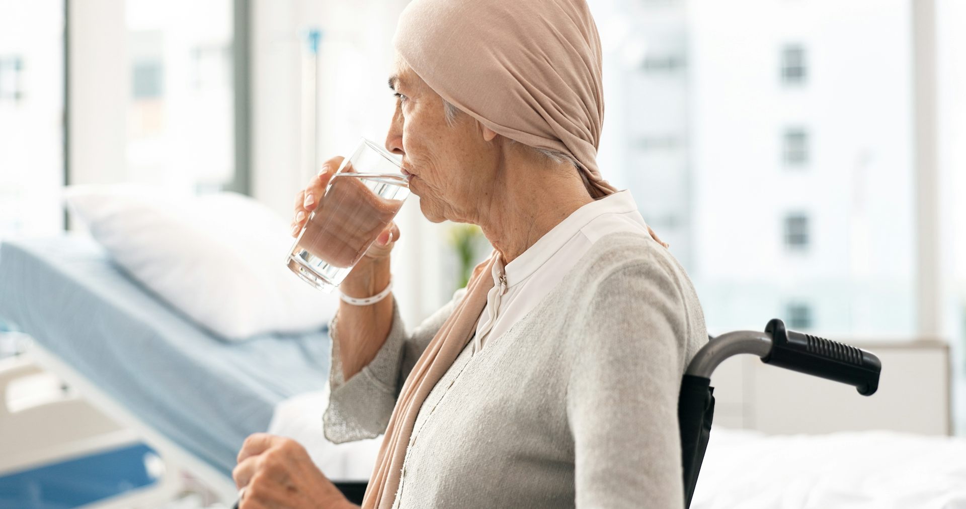 Une femme âgée, assise dans un fauteuil roulant, boit un verre d'eau.