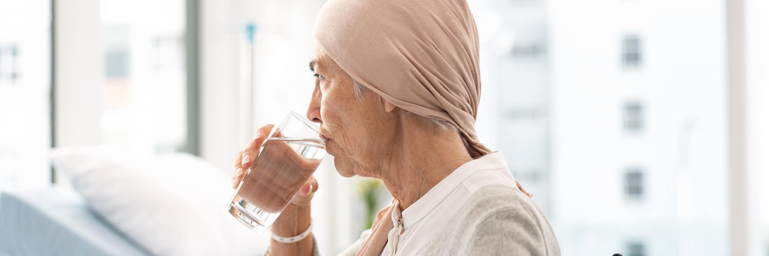 Une femme âgée, assise dans un fauteuil roulant, boit un verre d'eau.