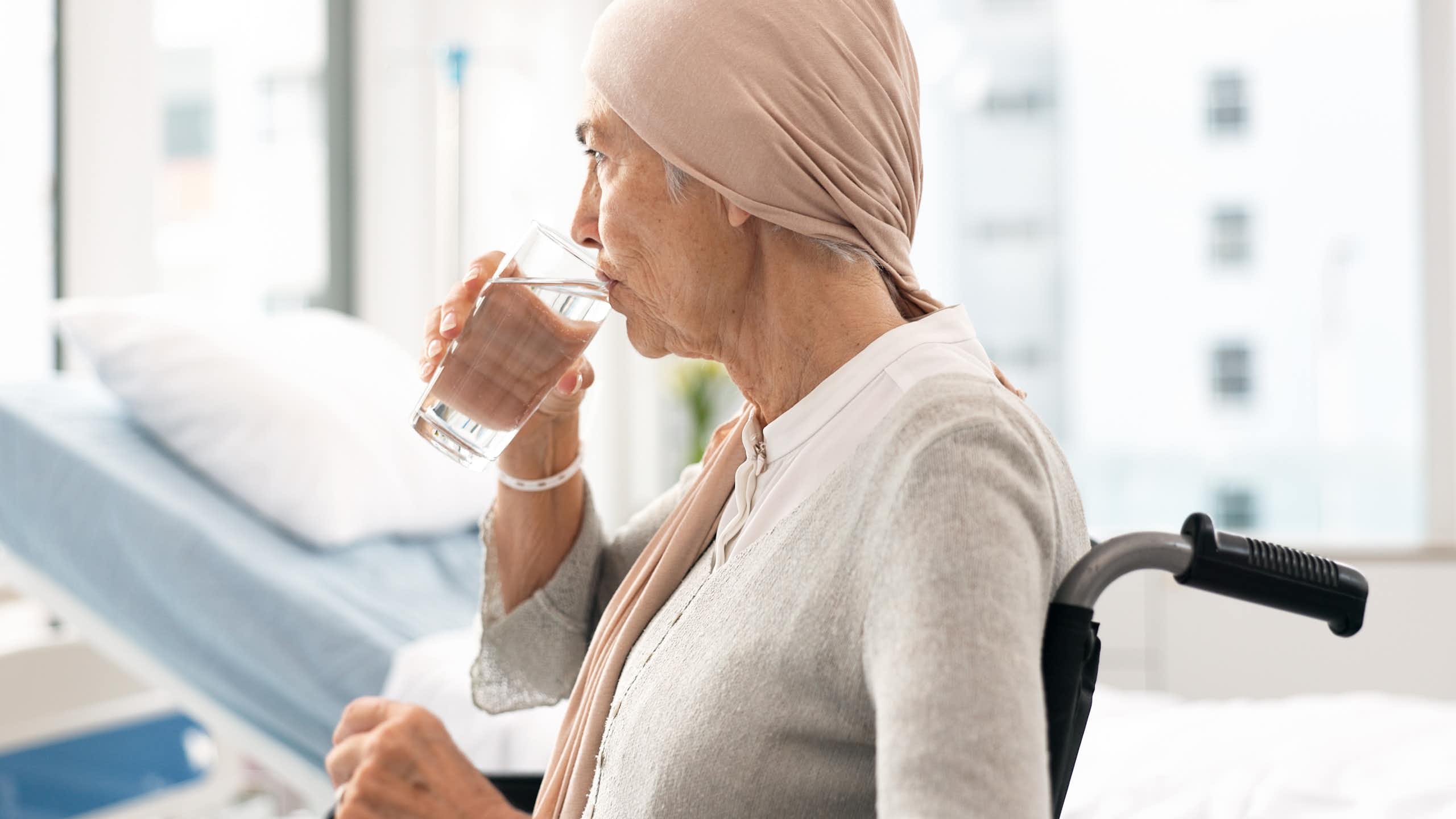 Une femme âgée, assise dans un fauteuil roulant, boit un verre d'eau.