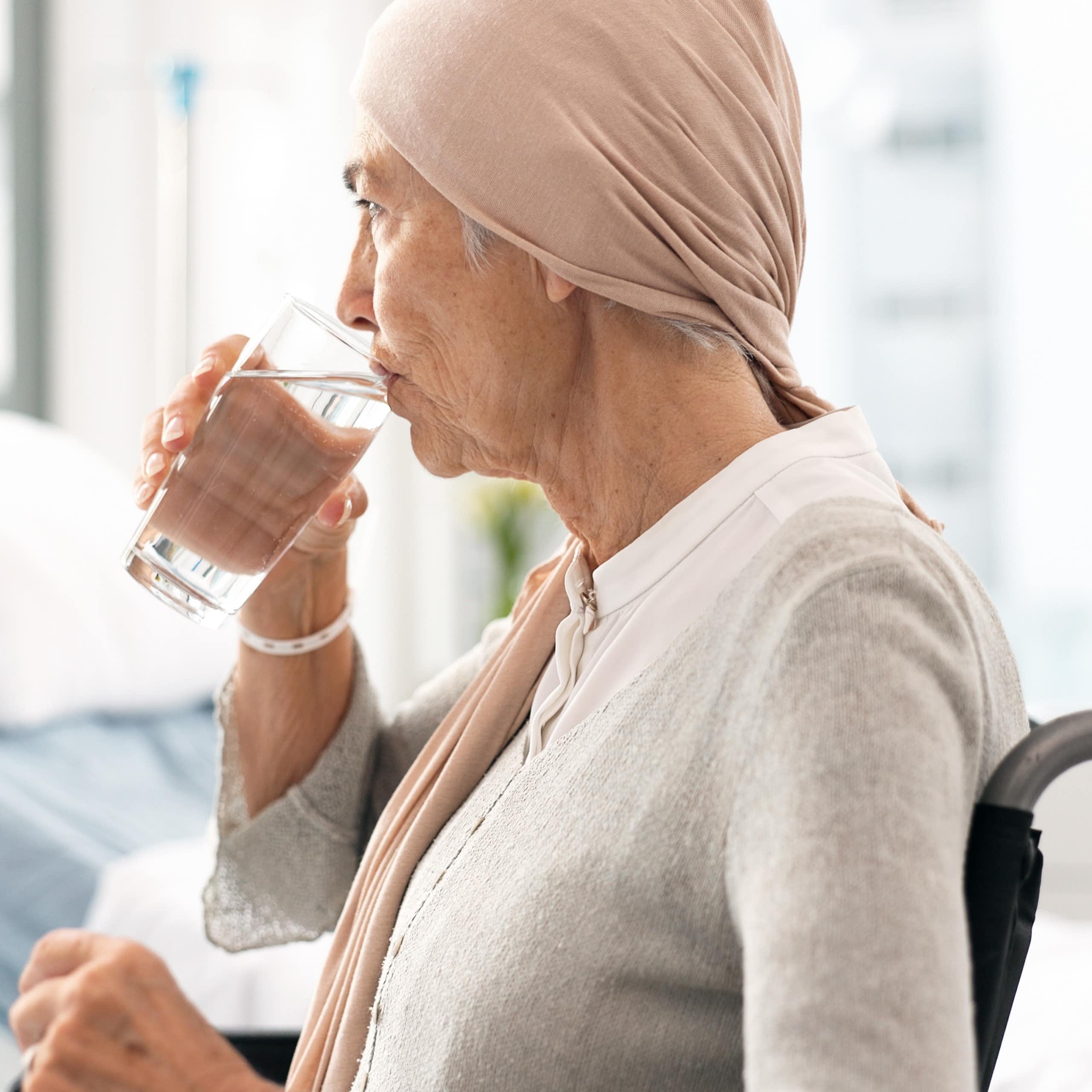 Une femme âgée, assise dans un fauteuil roulant, boit un verre d'eau.