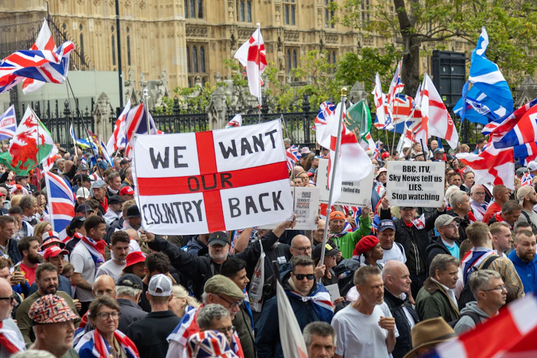 A large crowd of people with national flags of the UK, and a large St George's cross flag with 'we want our country back' written on it
