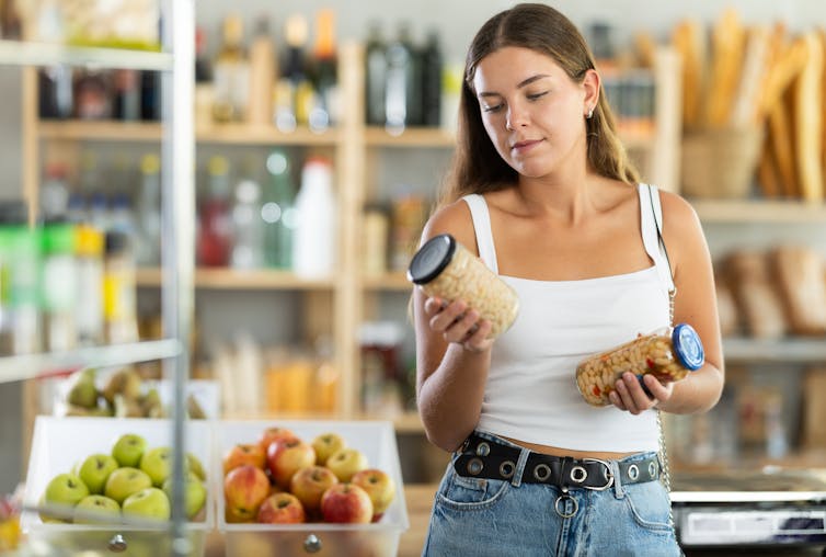 A young woman in a supermarket compares two jars of beans.