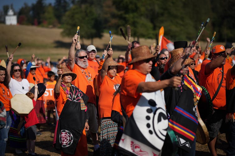Gente con tambores y camisetas naranjas caminan afuera.