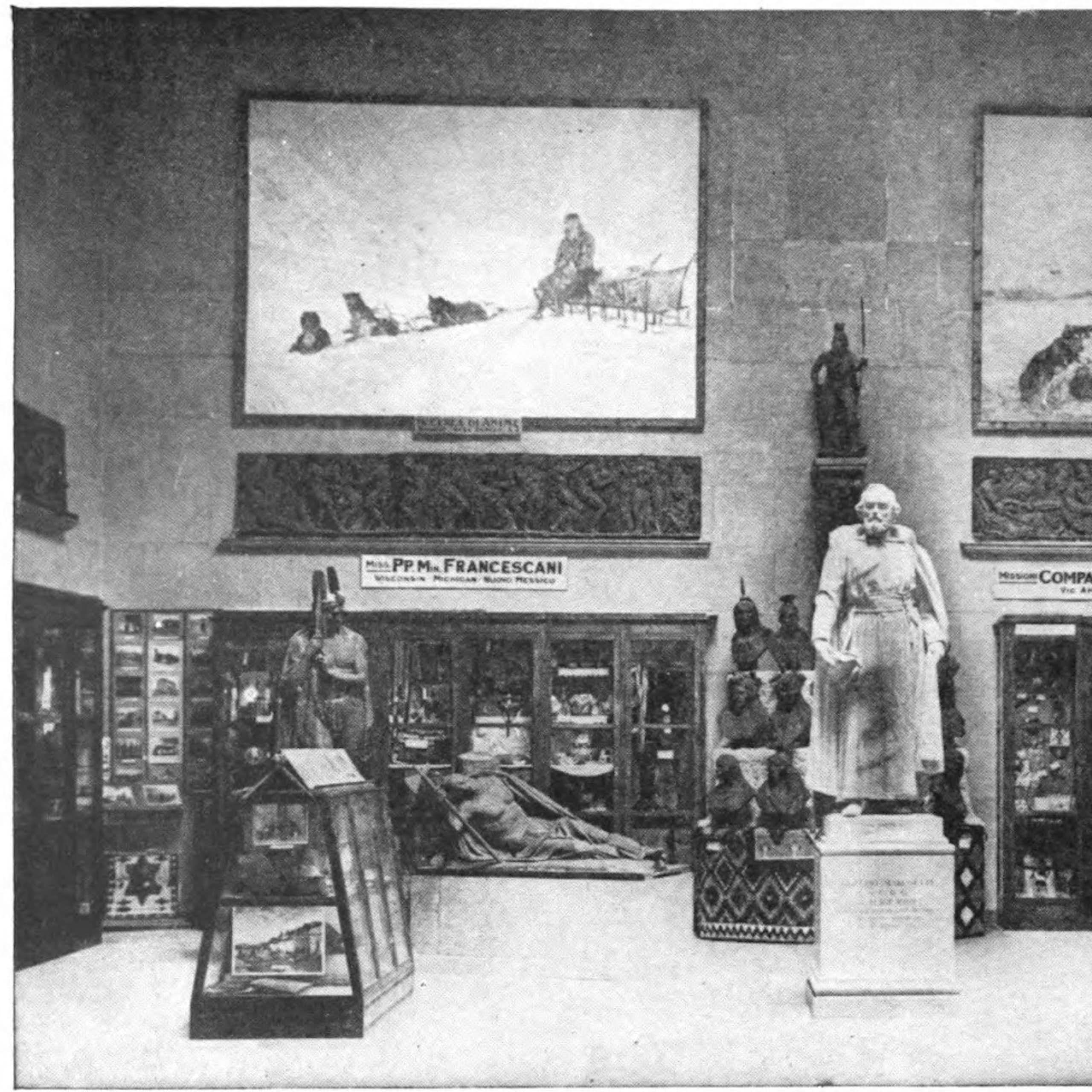 Statue on a pedestal surrounded by images on walls and some items in cases.