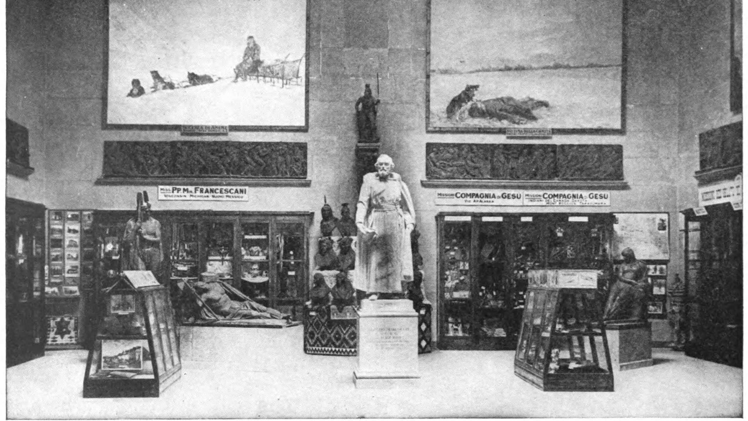 Statue on a pedestal surrounded by images on walls and some items in cases.