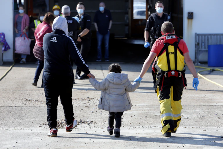 View from behind of a young refugee girl holding the hands of an RNLI volunteer and a male asylum seeker