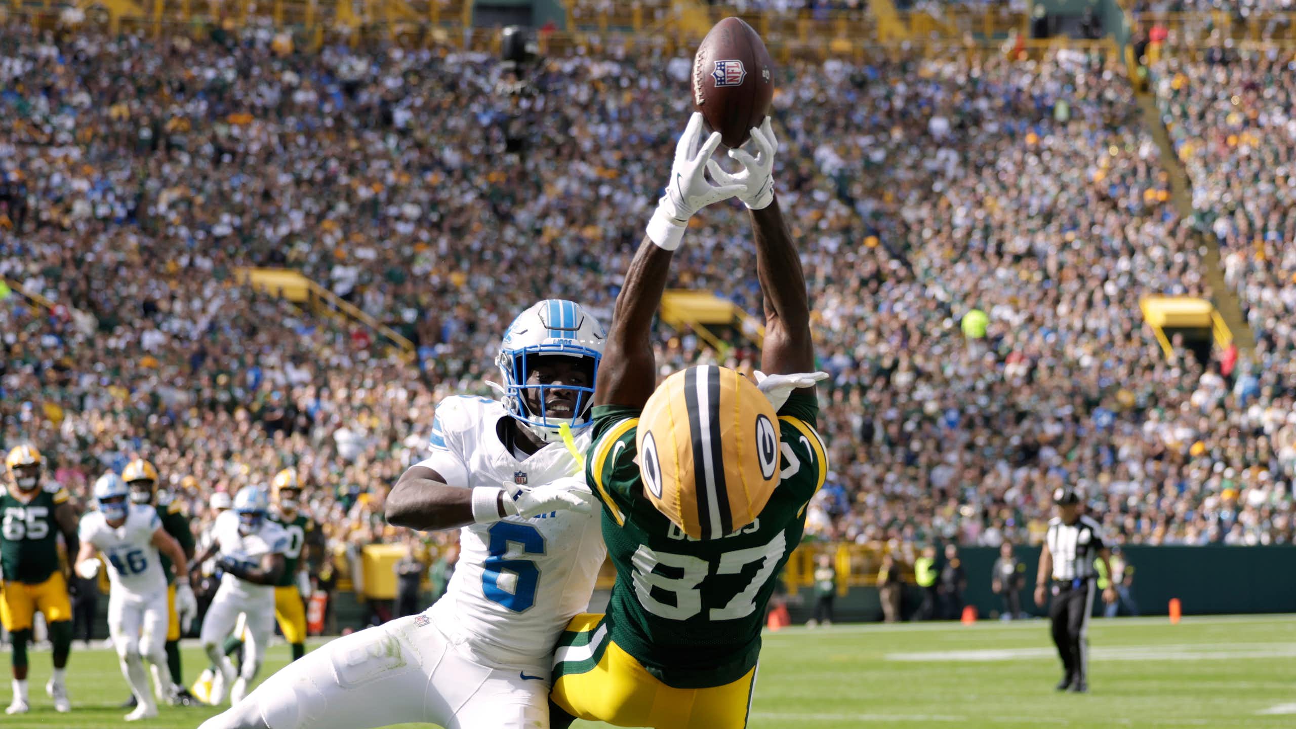 A player in a green and gold uniform falls backward while trying to catch a football.