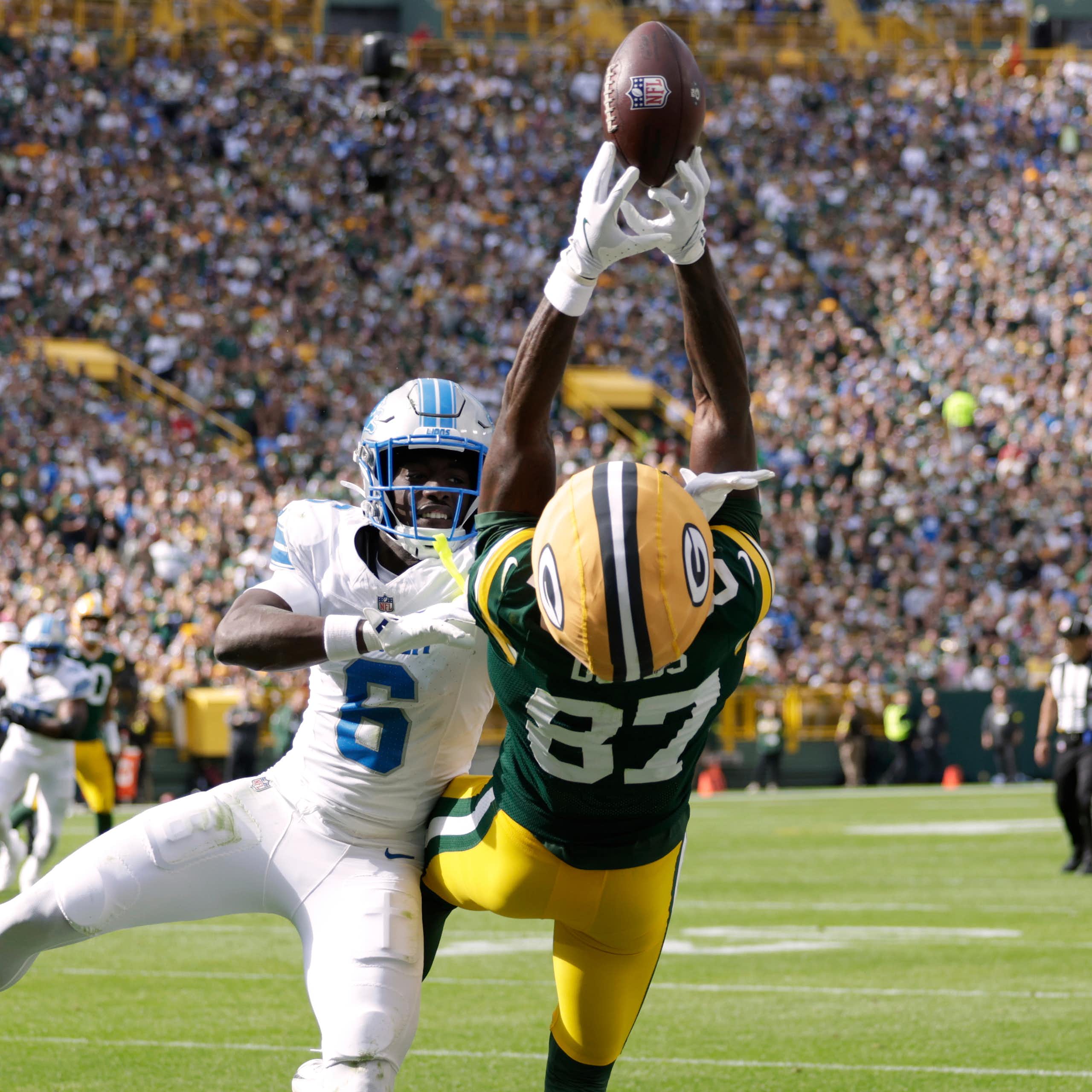 A player in a green and gold uniform falls backward while trying to catch a football.