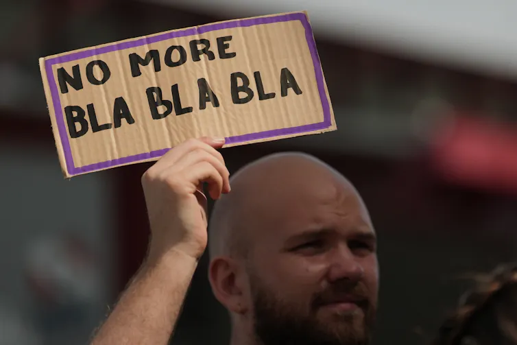 a man at a demonstration holds a small placard that reads: no more bla bla bla