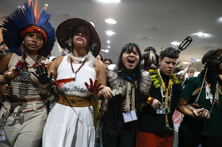 A line of protestors holding hands and shouting, wearing Indigenous jewellery