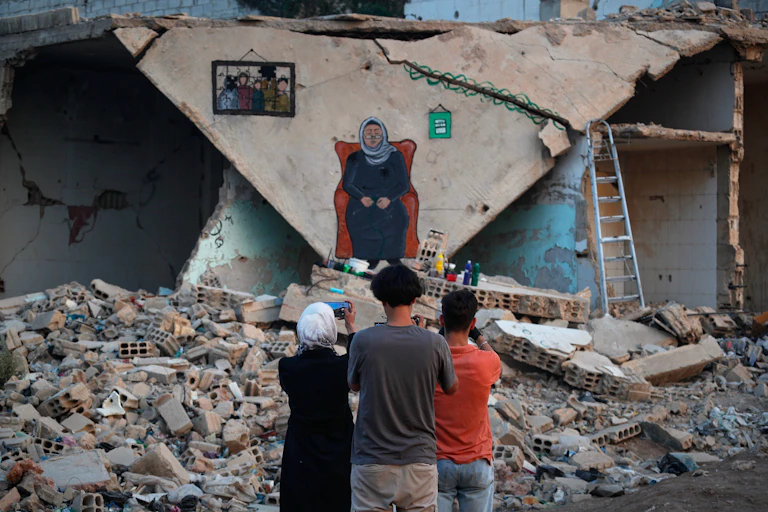 A group of people stand in front of a bombed house.