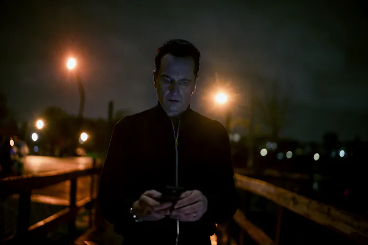 Nile in the half-dark under streetlights, looking at his phone.