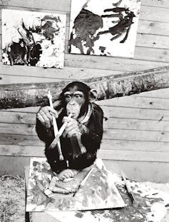 No, a monkey could not paint that image: What summary artwork finds in regards to the human thoughts 1 A black and white photo of a monkey holding brushes while sitting on some oil paintings.
