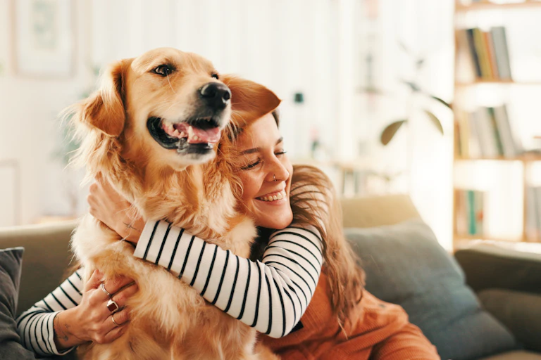 Woman hugging her golden retriever, both sat on a sofa