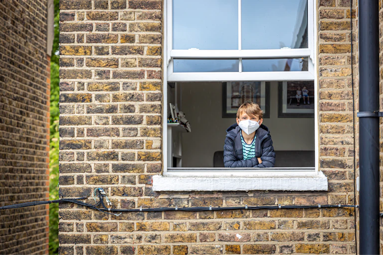 A boy wearing a mask stares wistfully out of a window during the lockdowns.
