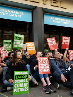 French protestors sitting down holding signs that say stop fossil fuel projects