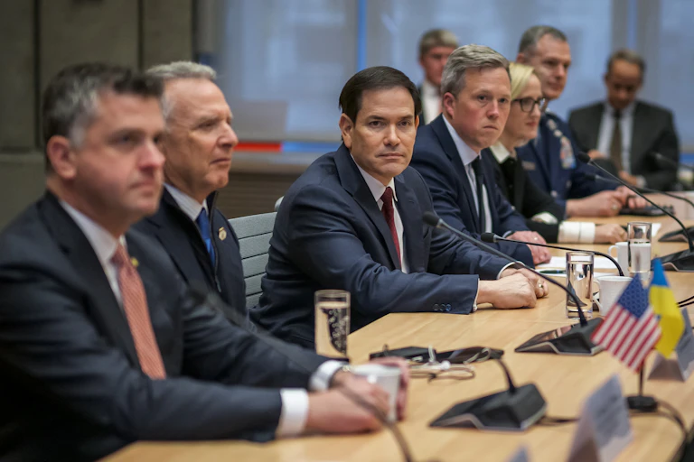 Many men in suits sitting along one side of a table.