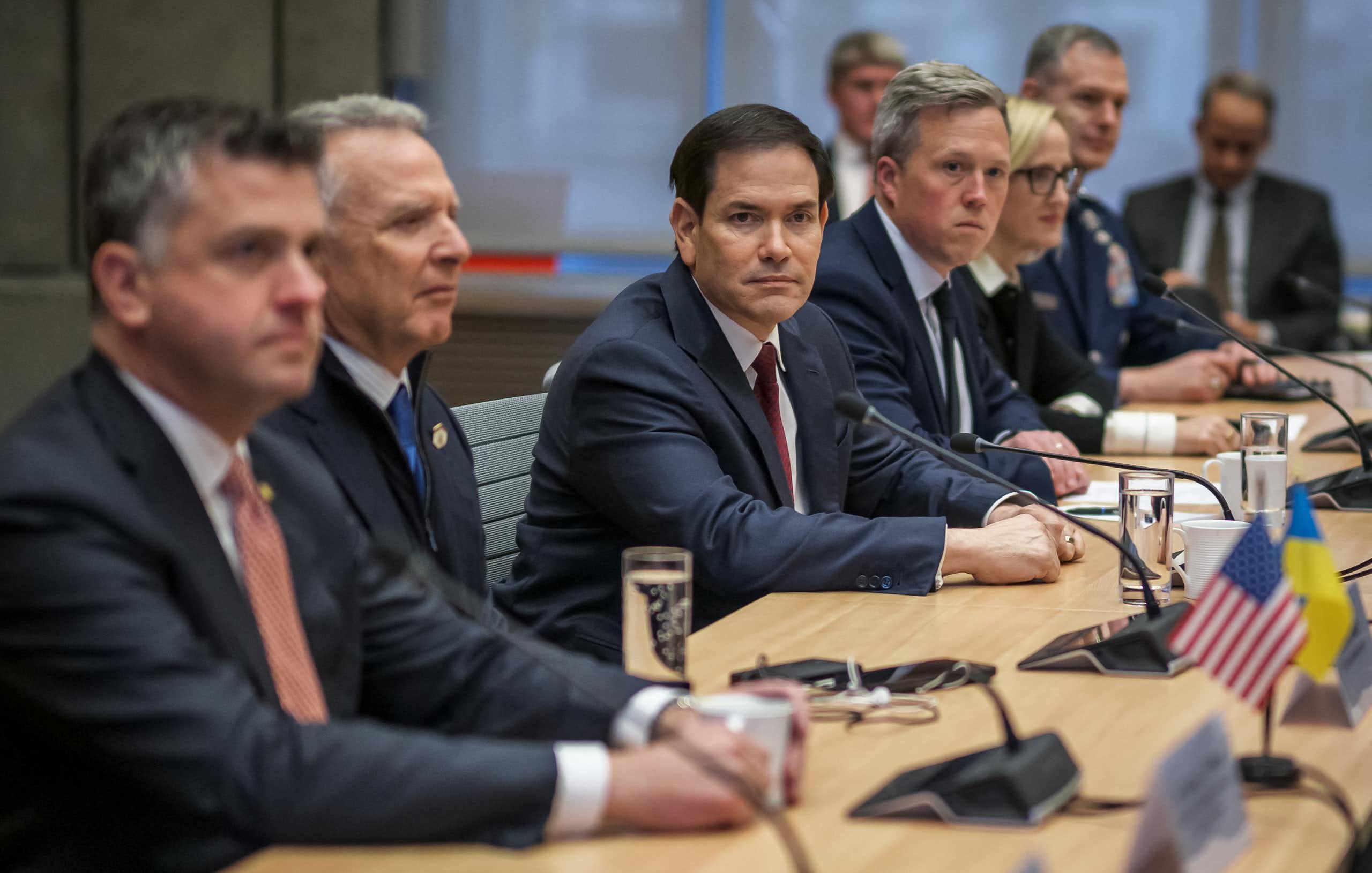 Many men in suits sitting along one side of a table.