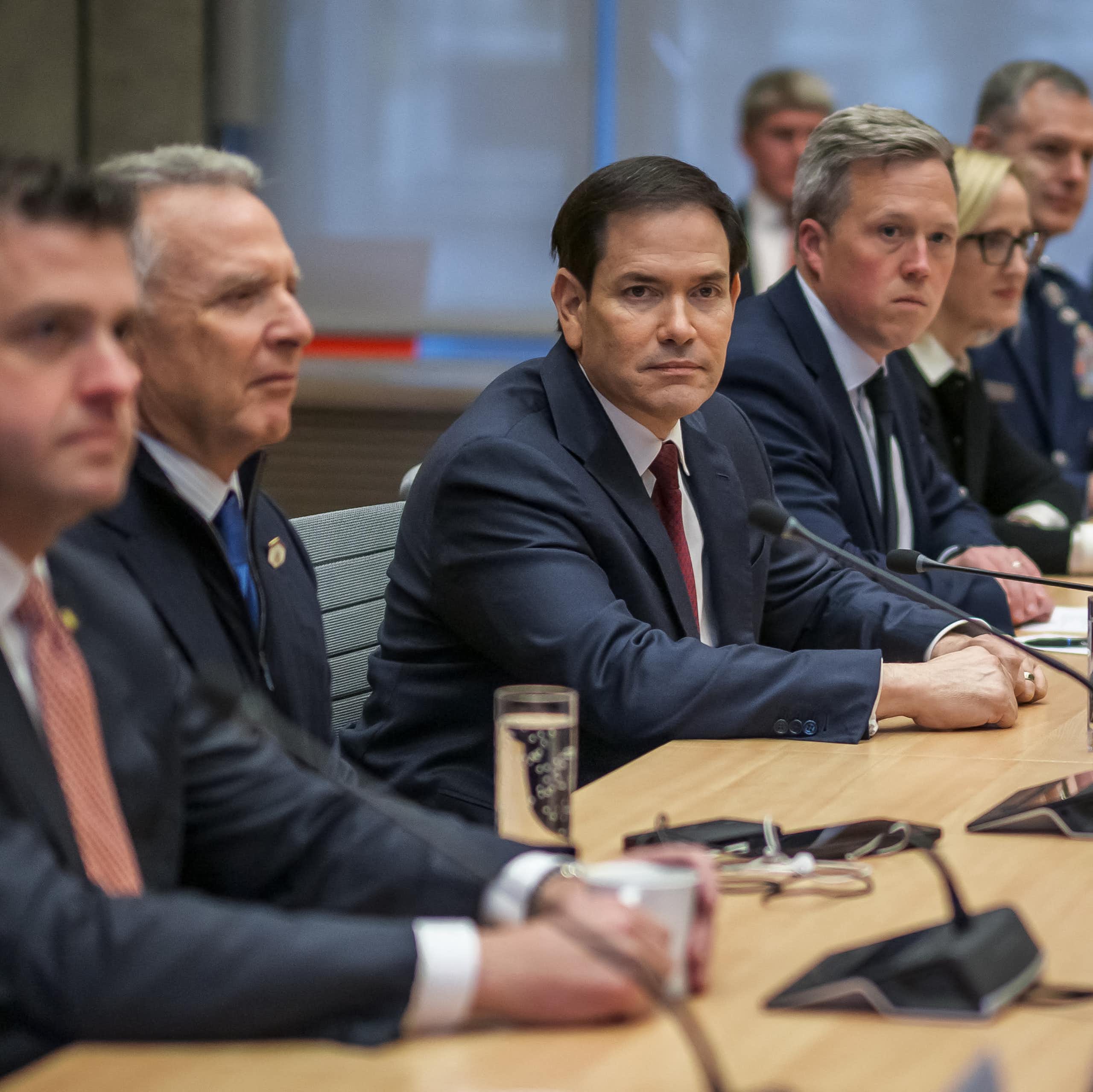 Many men in suits sitting along one side of a table.