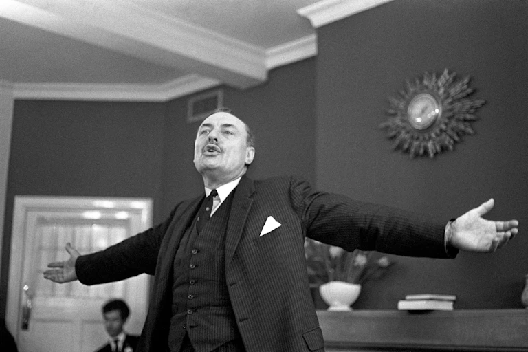 Man stands, arms spread wide during speech.