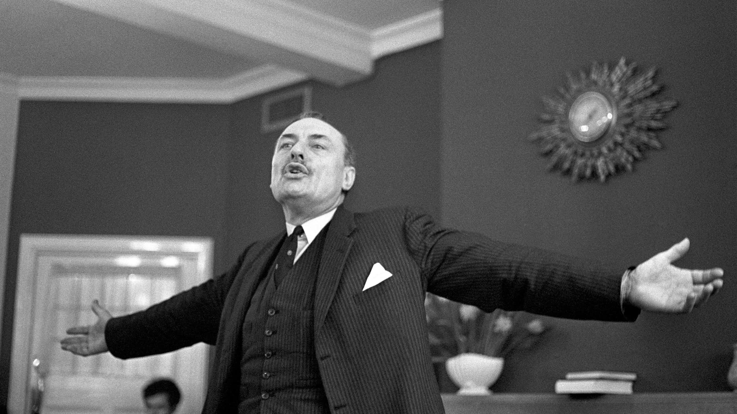 Man stands, arms spread wide during speech.
