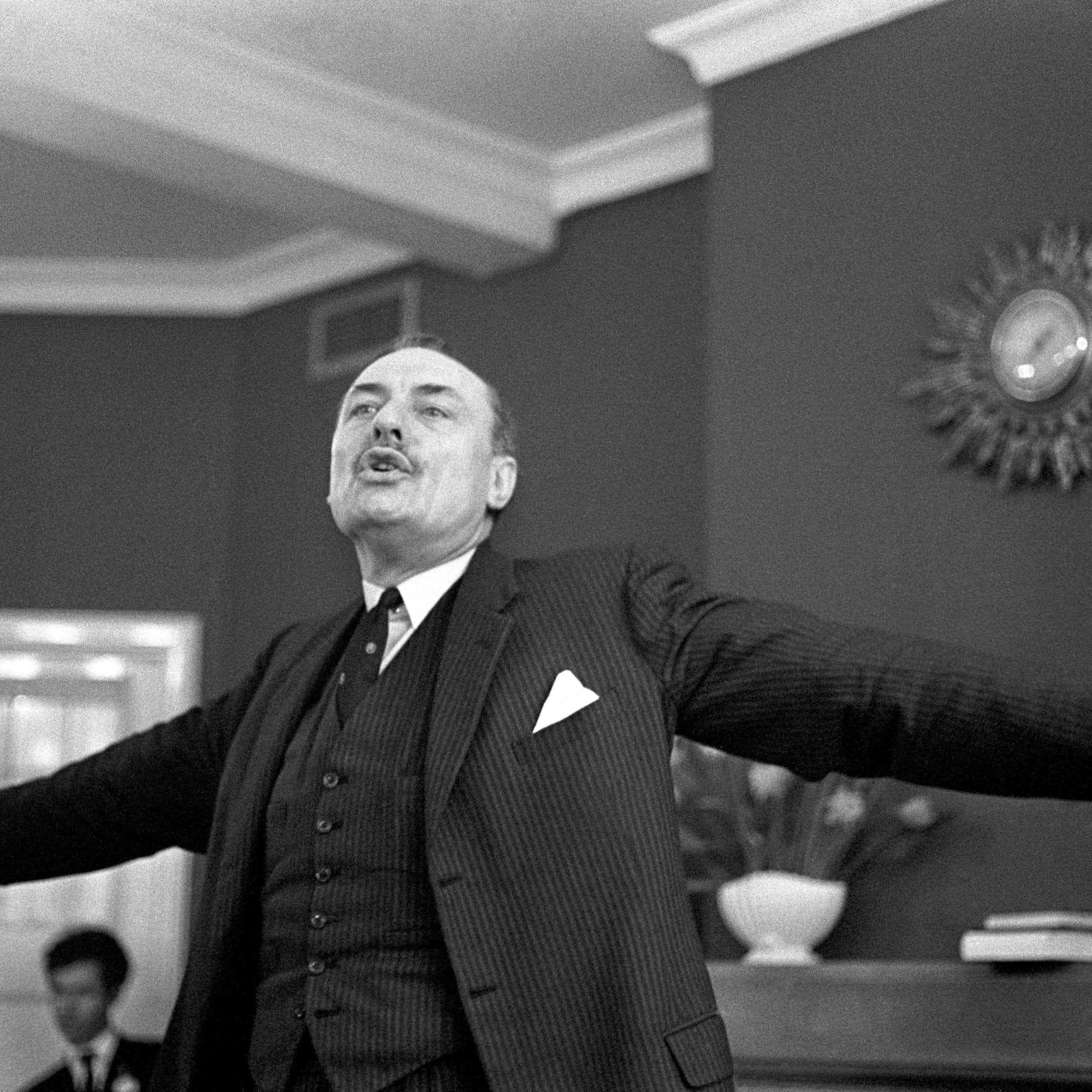 Man stands, arms spread wide during speech.