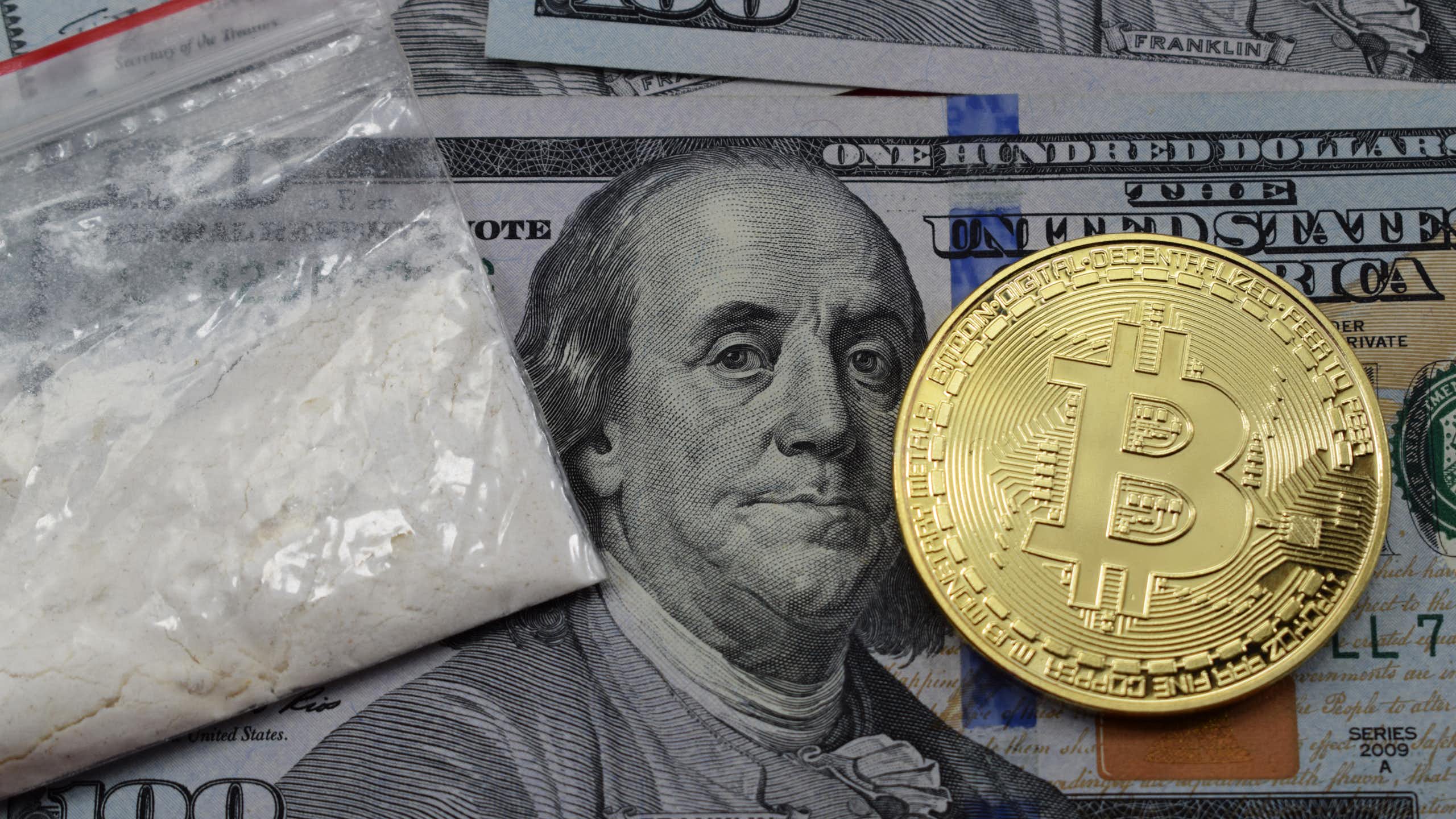 A hundred-dollar bill, a Bitcoin token, and a bag of cocaine.