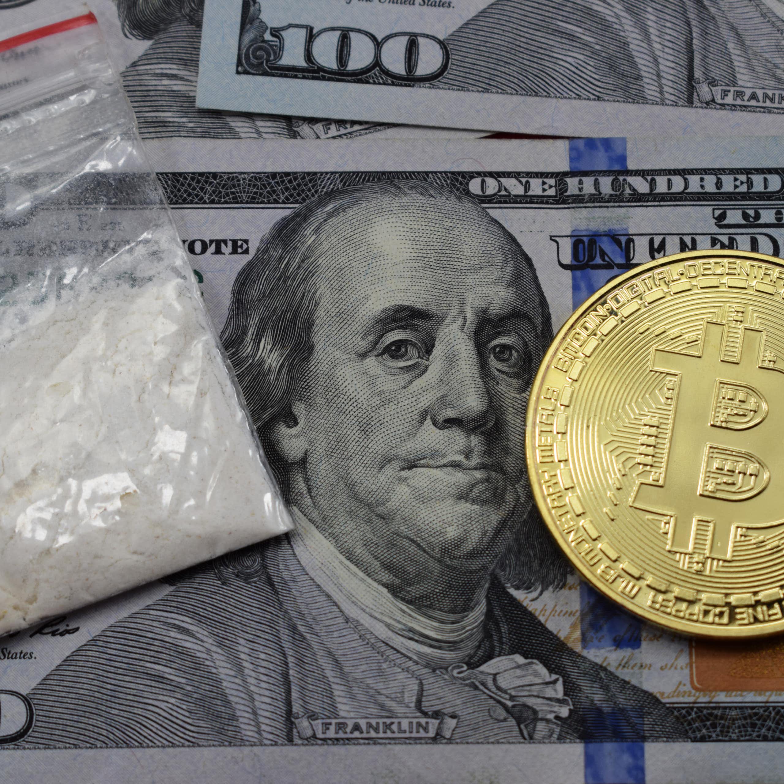 A hundred-dollar bill, a Bitcoin token, and a bag of cocaine.