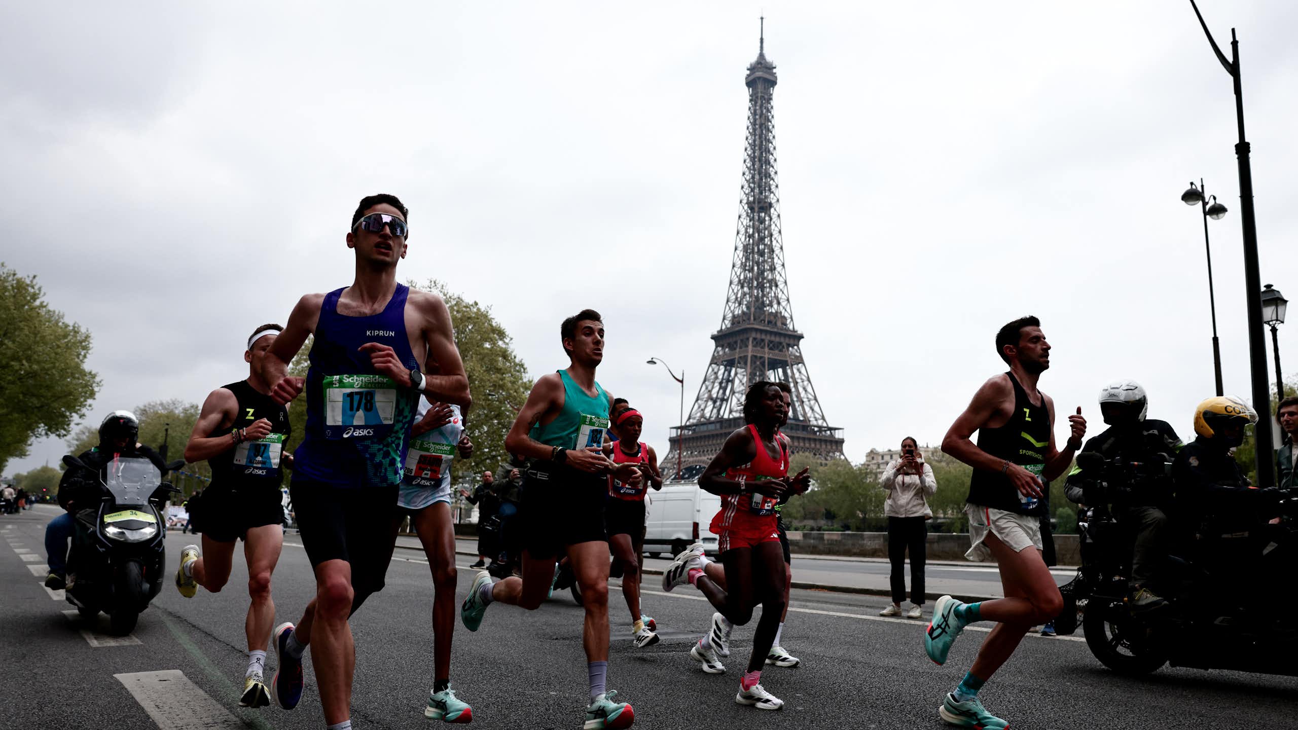 Amateur and professional runners during the Paris Marathon, with the Eiffel Tower visible in the background.