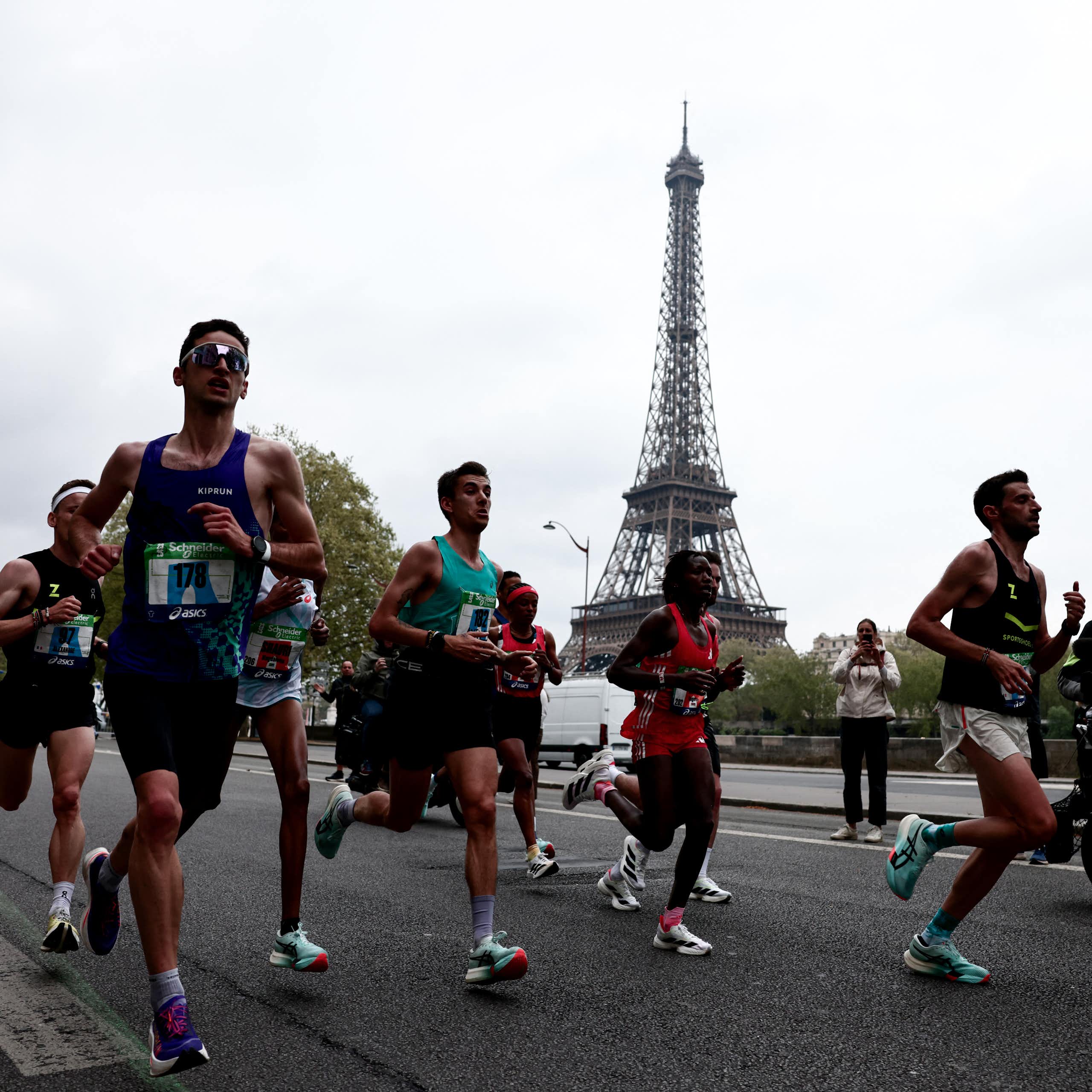 Amateur and professional runners during the Paris Marathon, with the Eiffel Tower visible in the background.