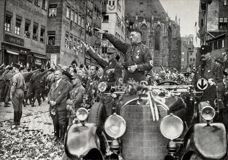 Adolf Hitler gives the Nazi salute from his car.
