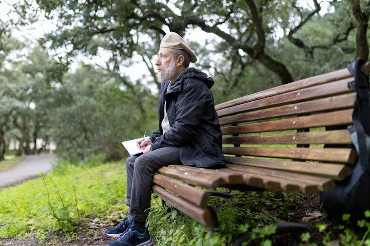 Man sat writing on a park bench