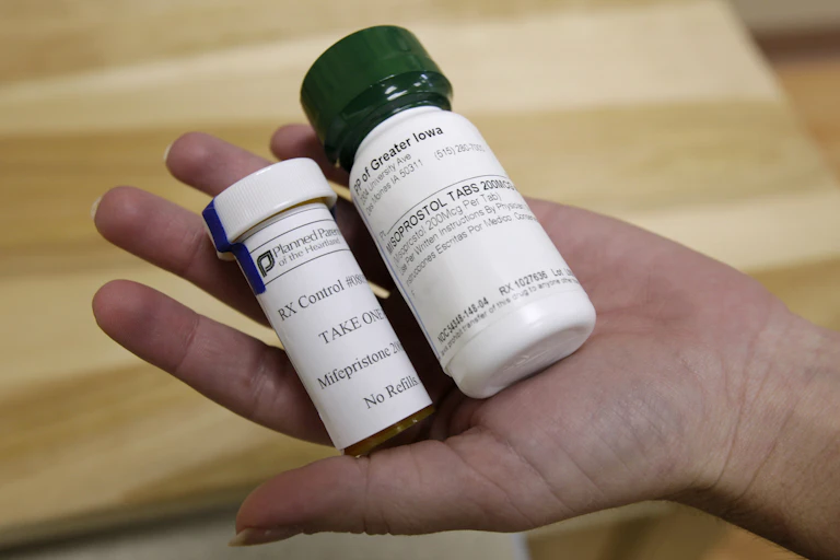Hand holding two pill bottles, one containing mifepristone and the other misoprostol.