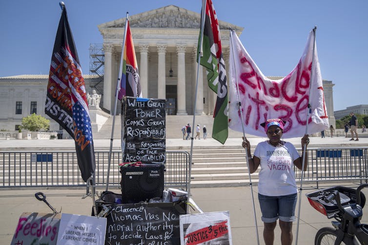 Woman outside the Supreme Court building holding an array of signs urging the Supreme Court to maintain access to telehealth abortion.